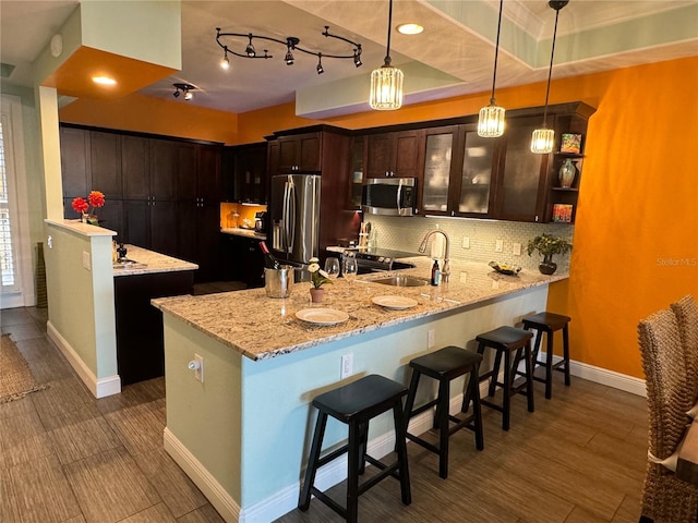 kitchen featuring sink, hanging light fixtures, light stone counters, kitchen peninsula, and appliances with stainless steel finishes