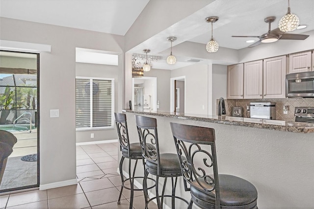 kitchen with light stone countertops, stainless steel appliances, tasteful backsplash, decorative light fixtures, and light tile patterned flooring