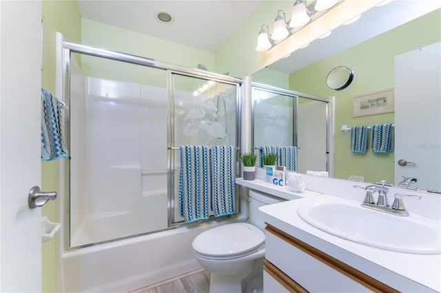 full bathroom with hardwood / wood-style floors, vanity, combined bath / shower with glass door, and toilet