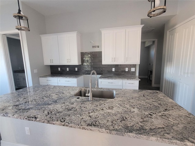 kitchen featuring backsplash, decorative light fixtures, white cabinetry, and sink