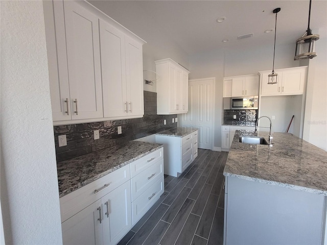 kitchen featuring sink, hanging light fixtures, backsplash, a kitchen island with sink, and white cabinets