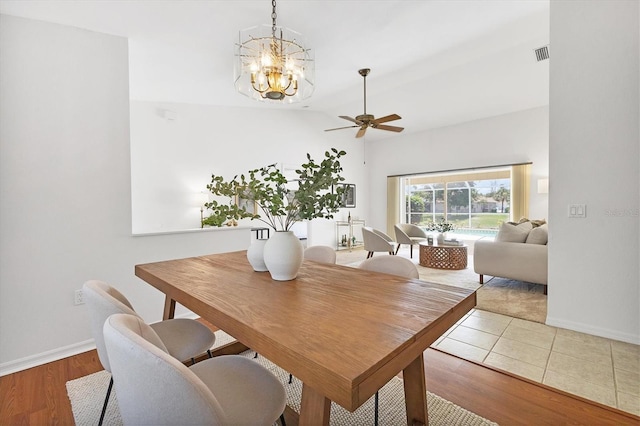 dining area with ceiling fan with notable chandelier, light wood-type flooring, and vaulted ceiling