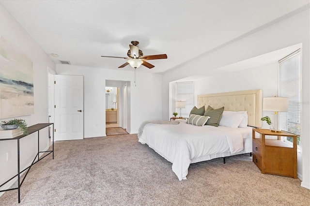 bedroom featuring a textured ceiling, ceiling fan, light carpet, and connected bathroom