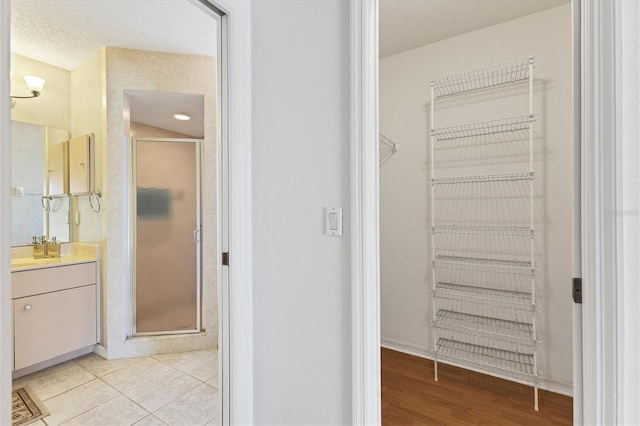 bathroom with tile patterned flooring, vanity, a shower with shower door, and a textured ceiling