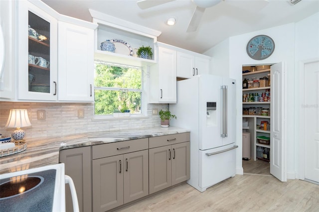 kitchen featuring light stone countertops, light wood-type flooring, tasteful backsplash, high end white fridge, and white cabinets