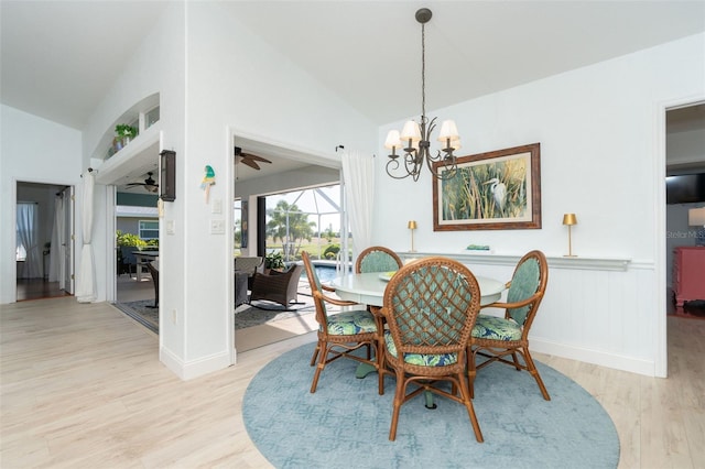 dining room featuring ceiling fan with notable chandelier, light wood-type flooring, and lofted ceiling