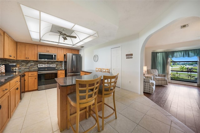 kitchen featuring light tile patterned floors, a breakfast bar, ceiling fan, appliances with stainless steel finishes, and backsplash