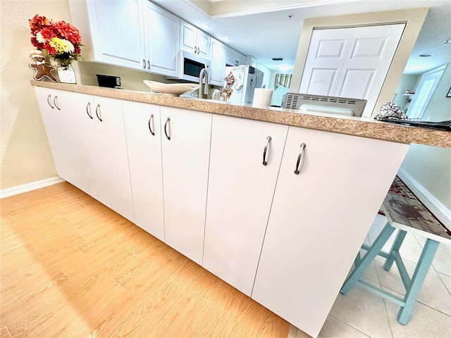 kitchen with white cabinetry, sink, white appliances, and light hardwood / wood-style flooring