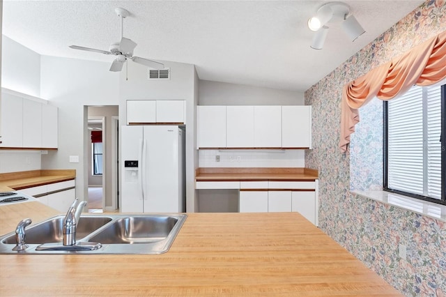 kitchen featuring lofted ceiling, sink, white fridge with ice dispenser, a textured ceiling, and white cabinetry