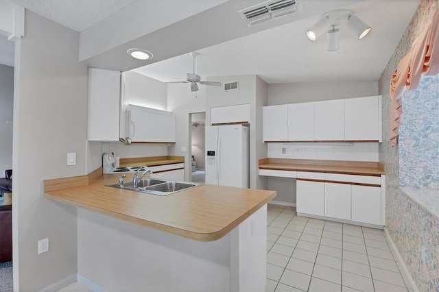 kitchen featuring kitchen peninsula, white cabinetry, white fridge with ice dispenser, and sink