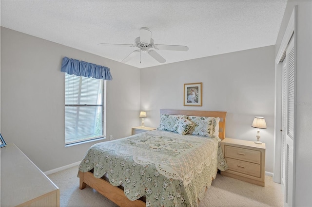 bedroom featuring ceiling fan, a closet, light carpet, and a textured ceiling