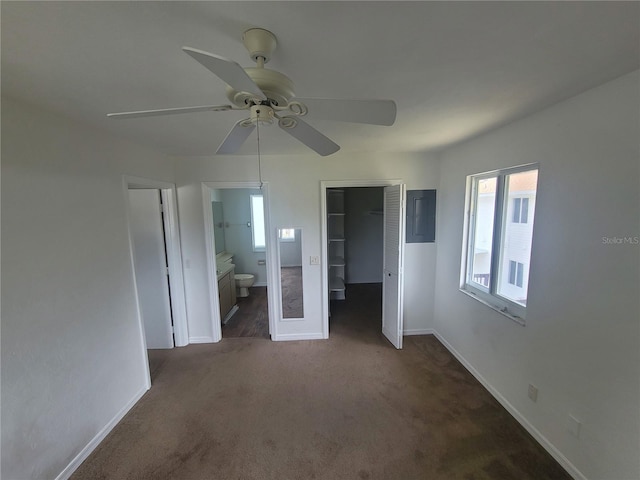 unfurnished bedroom with connected bathroom, dark colored carpet, and ceiling fan