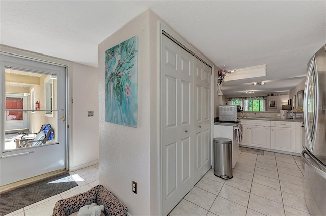 interior space with stainless steel fridge with ice dispenser, white cabinetry, a textured ceiling, and light tile patterned floors