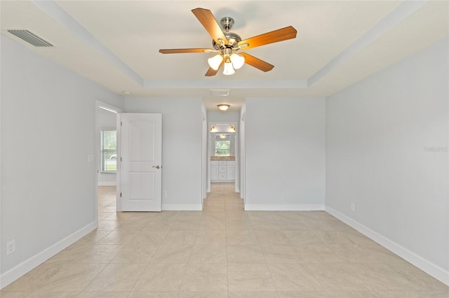 tiled empty room featuring a raised ceiling and ceiling fan