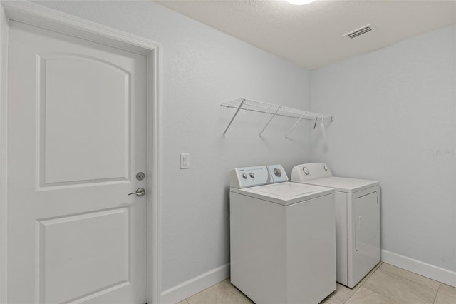 clothes washing area featuring light tile patterned floors, a textured ceiling, and separate washer and dryer