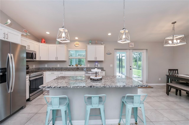 kitchen with white cabinetry, a kitchen island, decorative light fixtures, and appliances with stainless steel finishes