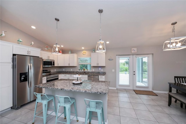 kitchen featuring stainless steel appliances, vaulted ceiling, white cabinets, a center island, and hanging light fixtures