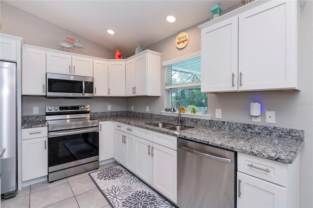 kitchen with light stone countertops, white cabinetry, sink, stainless steel appliances, and lofted ceiling