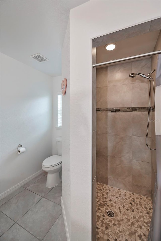 bathroom featuring tile patterned flooring, toilet, and tiled shower