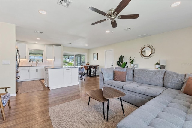 living room featuring wood-type flooring, ceiling fan, and sink