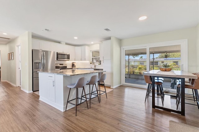 kitchen featuring a breakfast bar area, light hardwood / wood-style flooring, light stone counters, white cabinetry, and stainless steel appliances