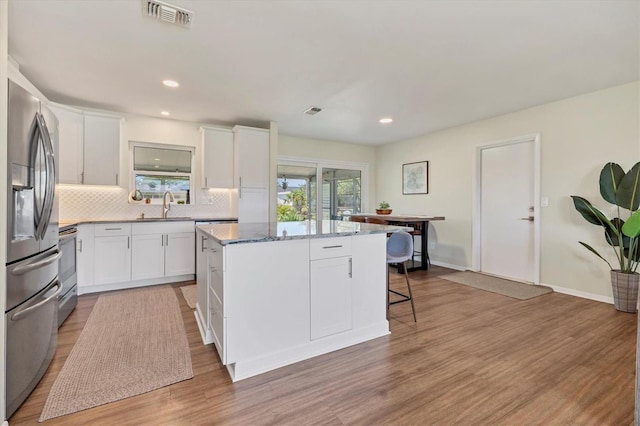 kitchen with appliances with stainless steel finishes, sink, stone countertops, a center island, and white cabinetry