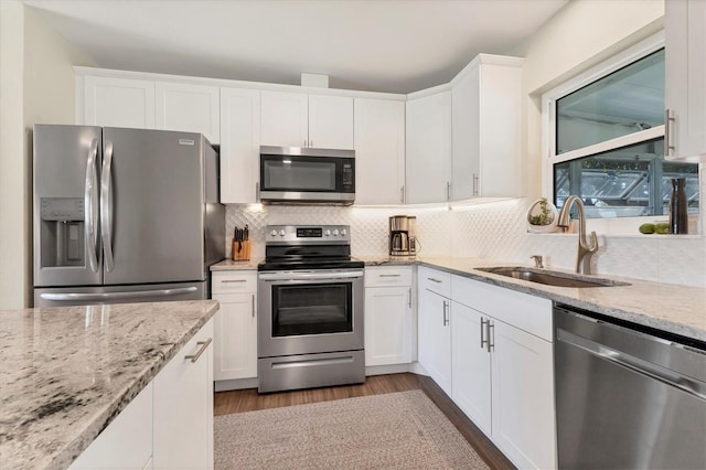 kitchen with light stone countertops, appliances with stainless steel finishes, sink, light hardwood / wood-style flooring, and white cabinets