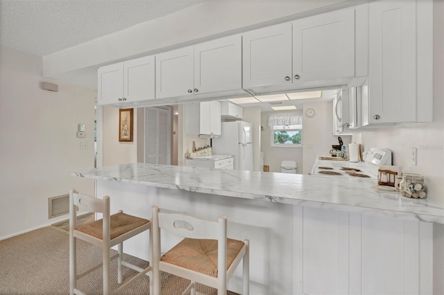 kitchen featuring white appliances, a breakfast bar, carpet, white cabinets, and kitchen peninsula