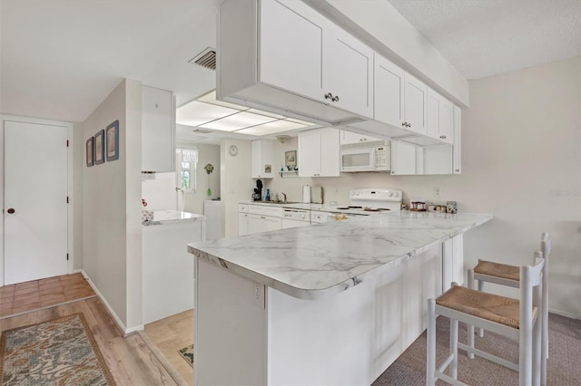 kitchen featuring white appliances, a kitchen breakfast bar, white cabinets, kitchen peninsula, and light wood-type flooring