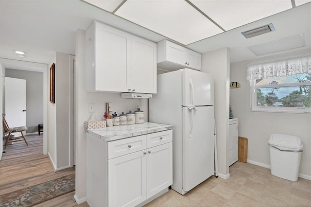 kitchen with white refrigerator, washer / dryer, light stone countertops, and white cabinets