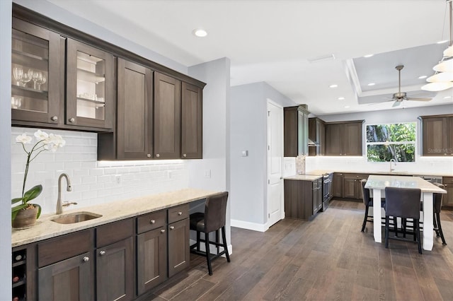 kitchen featuring ceiling fan, a tray ceiling, decorative backsplash, sink, and dark hardwood / wood-style floors