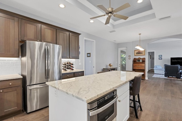 kitchen featuring wood-type flooring, decorative backsplash, a kitchen island, and stainless steel appliances