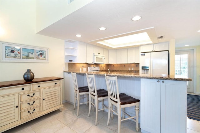 kitchen with white appliances, white cabinetry, dark stone counters, and backsplash