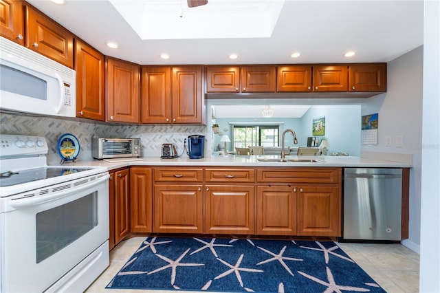 kitchen with decorative backsplash, a skylight, white appliances, sink, and light tile patterned flooring