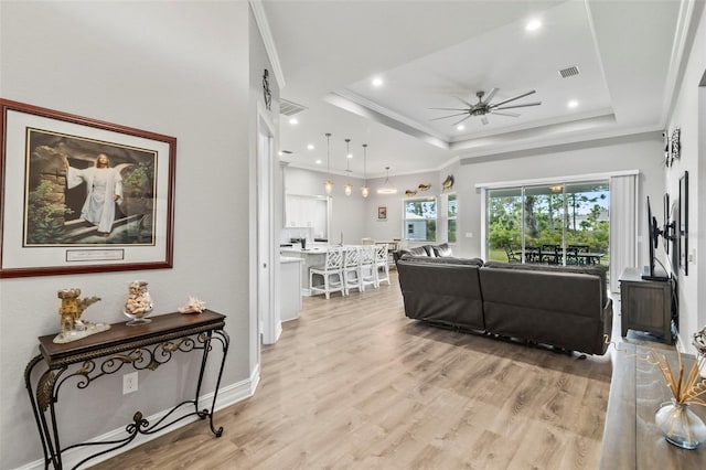 living room featuring ceiling fan, light hardwood / wood-style floors, crown molding, and a tray ceiling