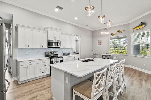 kitchen with light stone countertops, appliances with stainless steel finishes, white cabinetry, hanging light fixtures, and an island with sink