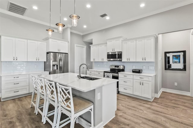 kitchen with appliances with stainless steel finishes, sink, pendant lighting, a center island with sink, and white cabinetry