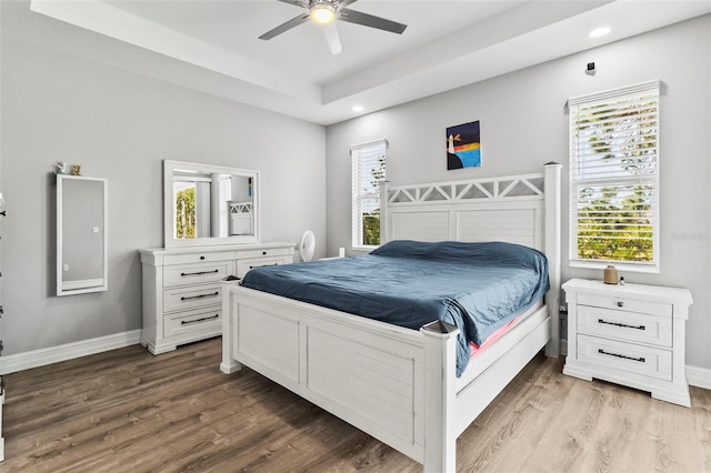 bedroom with hardwood / wood-style floors, ceiling fan, and a tray ceiling