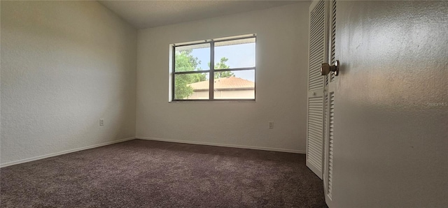 unfurnished room with vaulted ceiling and dark colored carpet