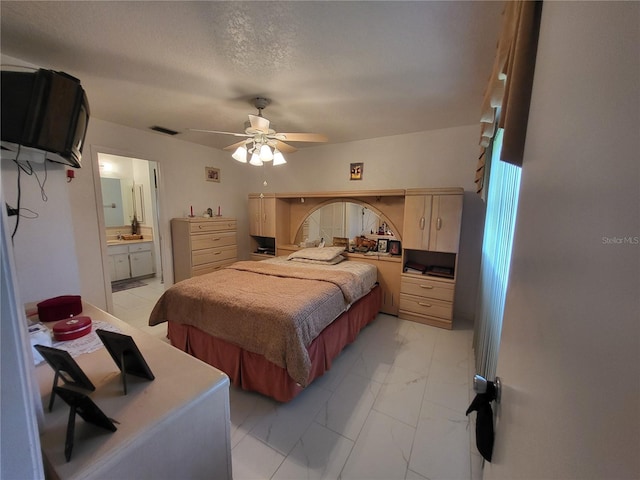 bedroom with ceiling fan, ensuite bath, and a textured ceiling