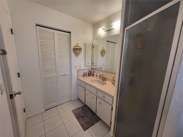 bathroom with a textured ceiling, tile patterned flooring, a shower with shower door, and vanity