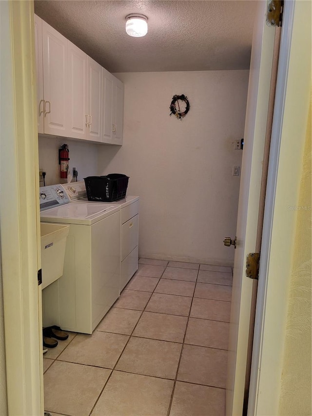 laundry room featuring light tile patterned floors, washing machine and dryer, a textured ceiling, and cabinets