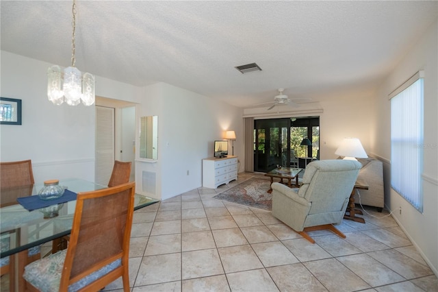 tiled living room with ceiling fan with notable chandelier and a textured ceiling