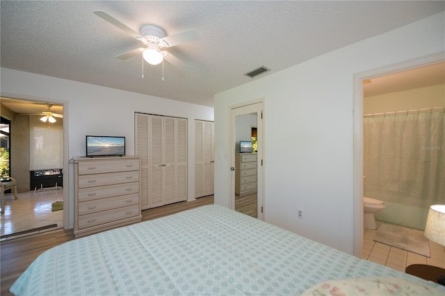 tiled bedroom with a textured ceiling, ensuite bathroom, ceiling fan, and two closets