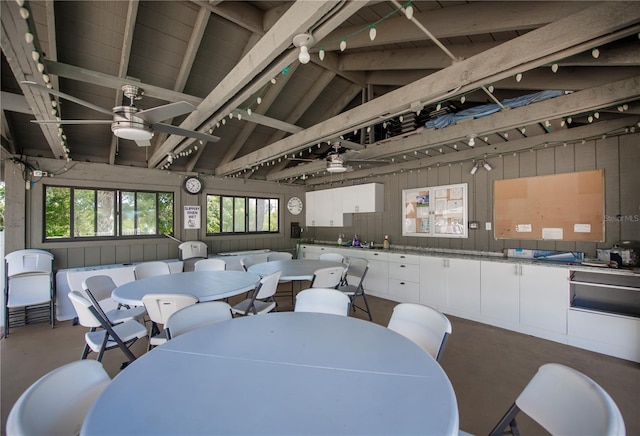 dining area with concrete flooring, ceiling fan, wooden walls, and lofted ceiling with beams