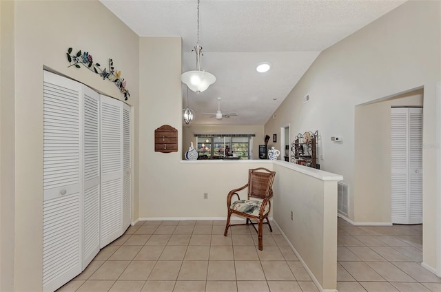 interior space with lofted ceiling, a textured ceiling, light tile patterned floors, and ceiling fan