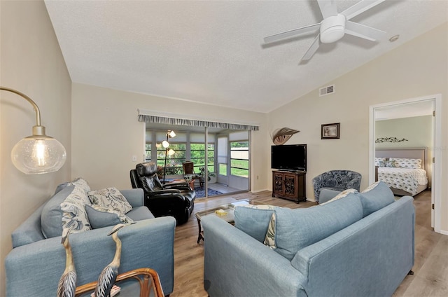 living room featuring a textured ceiling, vaulted ceiling, light wood-type flooring, and ceiling fan