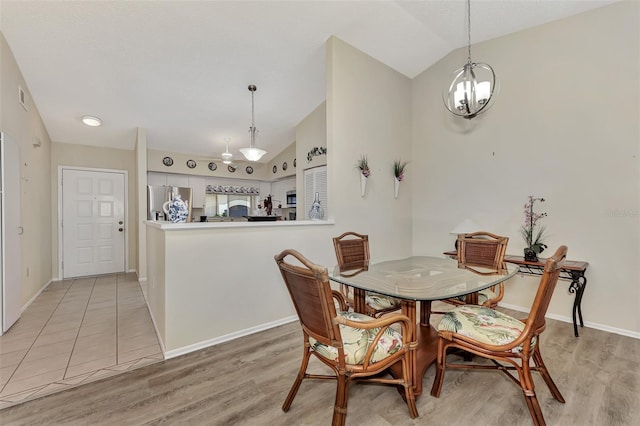 dining space with a chandelier, light wood-type flooring, and vaulted ceiling