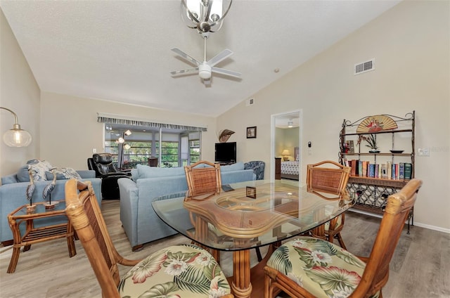 dining area with high vaulted ceiling, light wood-type flooring, ceiling fan with notable chandelier, and a textured ceiling