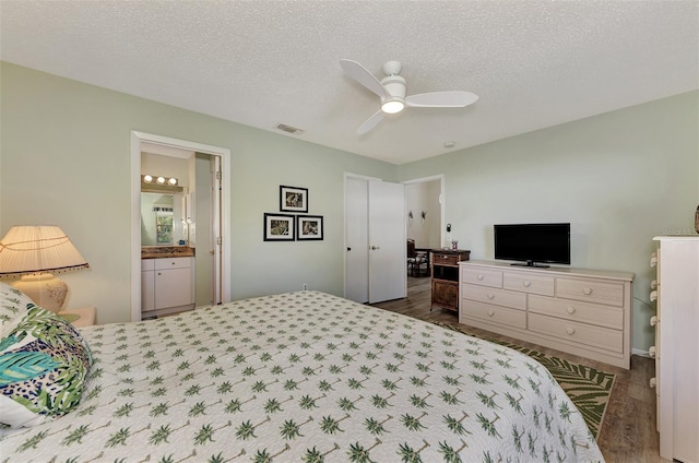 bedroom with a textured ceiling, connected bathroom, ceiling fan, and dark wood-type flooring